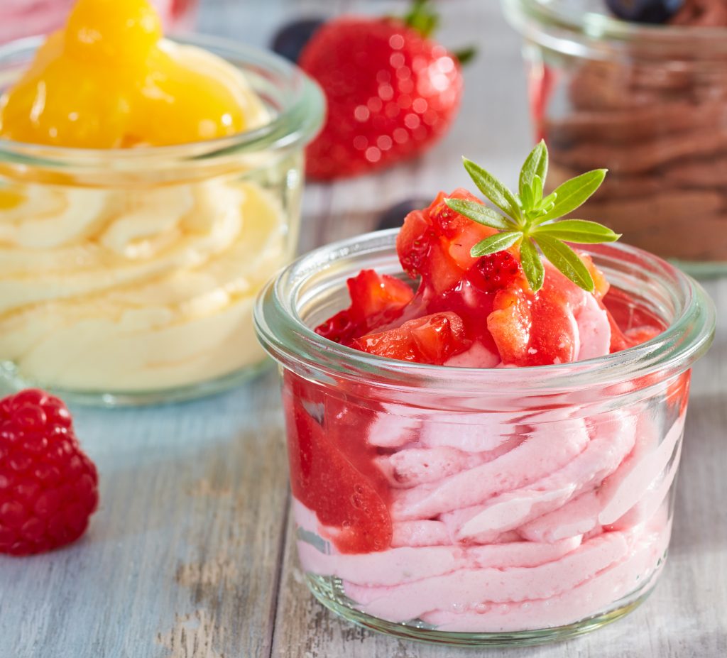 Kleine Gläschen, gefüllt mit Dessertcremes, im Vordergrund Erdbeer-Creme garniert mit Erdbeerpüree, im Hintergrund Schoko und Mango