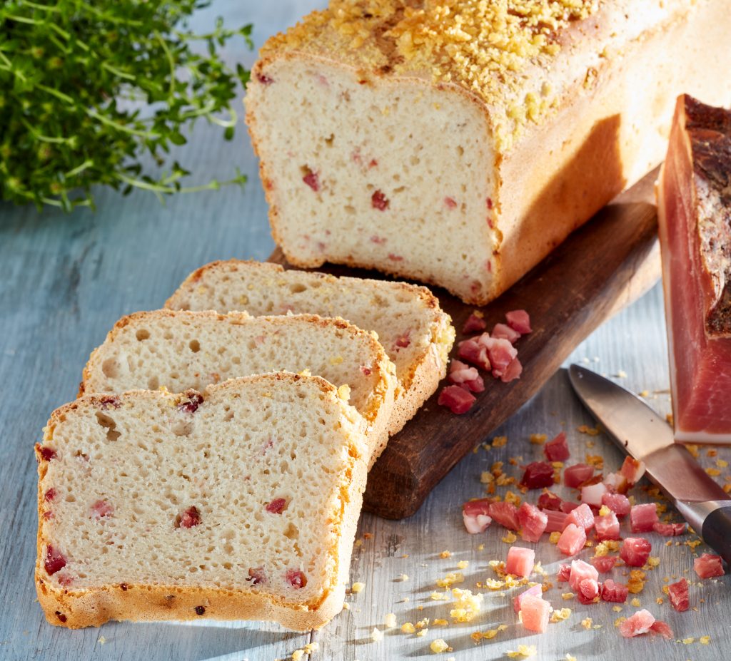 Easy White - helles Brot, im Kasten gebacken mit kleinen Speckwürfeln darin. Angeschnitten, 3 Scheiben liegen auf dem Brett
