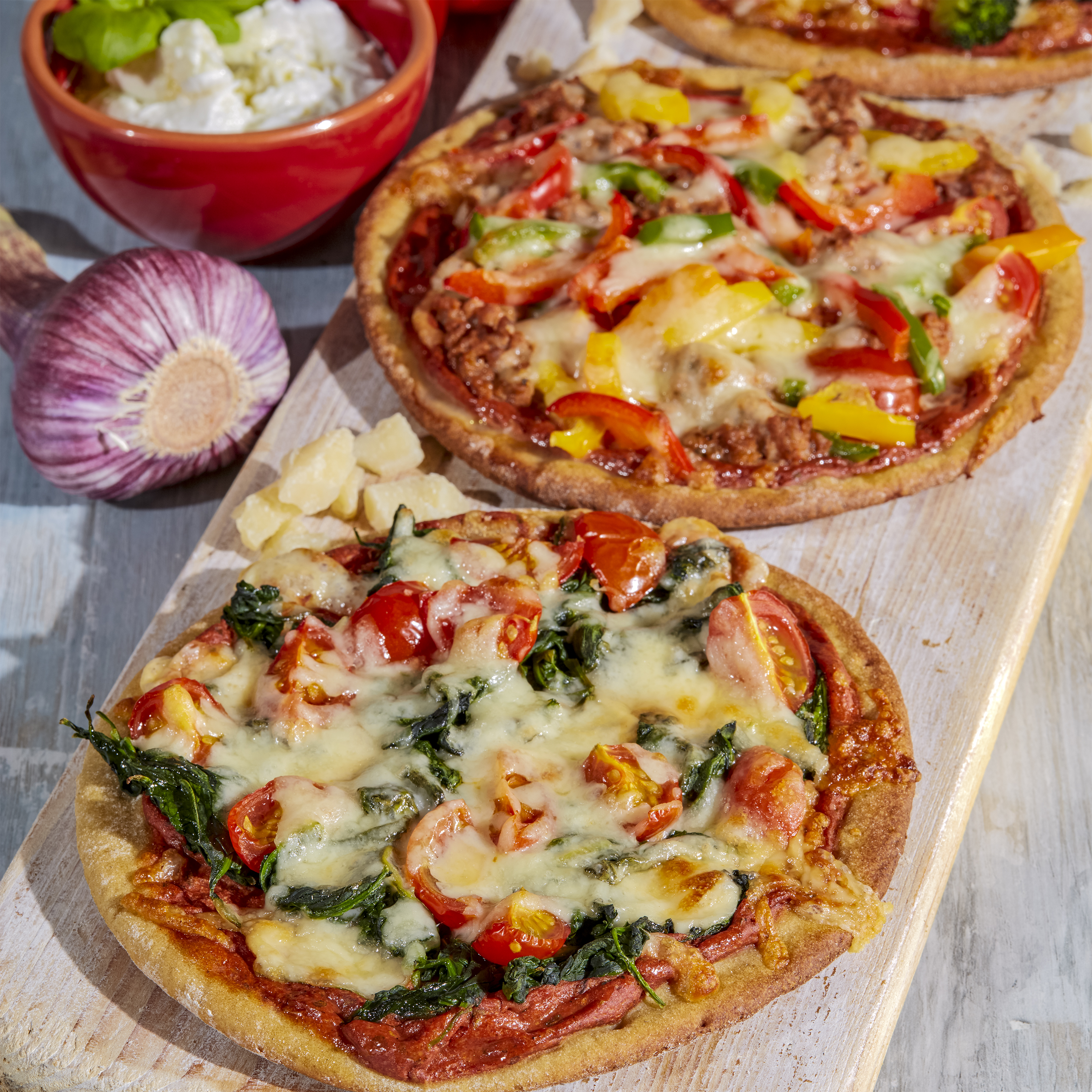 Protein Pizza, belegt mit Spinat und Tomaten, dahinter Proteinpizza belegt mit bunter Paprika
