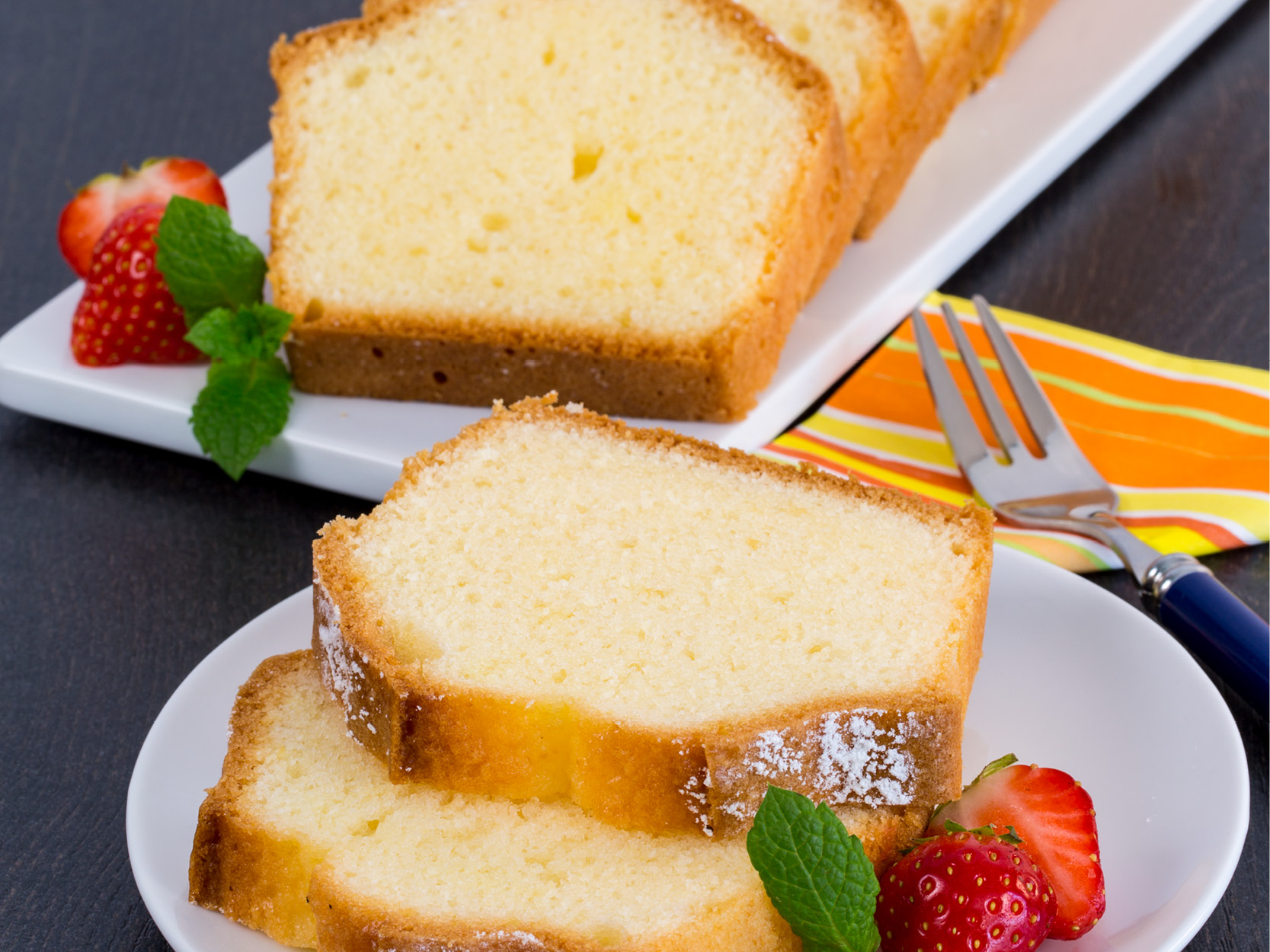 Glutenfreier heller Rührkuchen, im Kasten gebacken. Zwei Stücke auf einem Teller, garniert mit frischen Erdbeeren