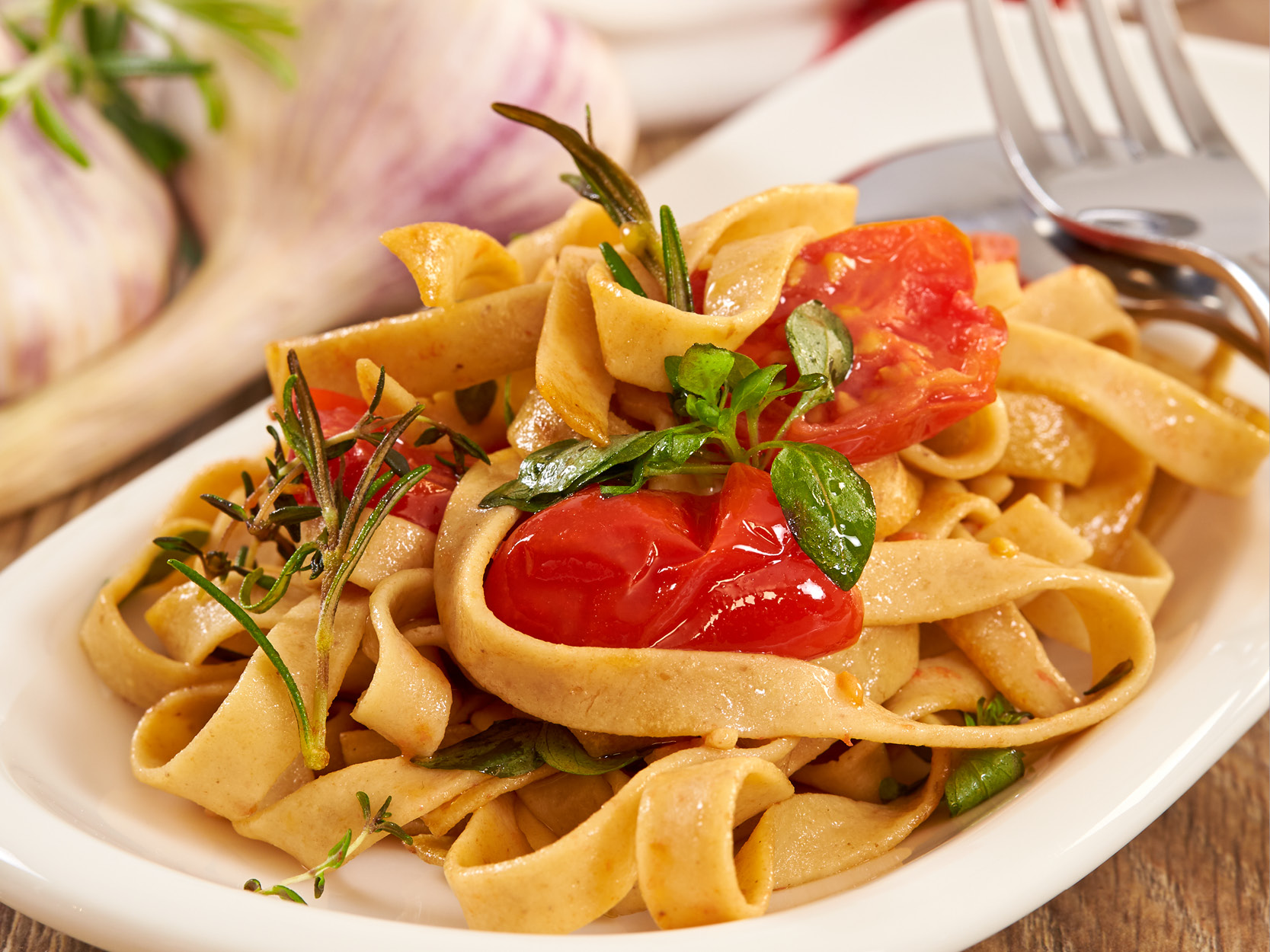 Proteinpasta, gekocht und auf Teller angerichtet mit Tomate, Basilikum, Rosmarin